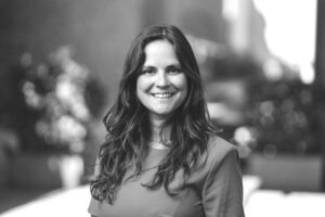 Black and white portrait of Catrien Janssen, smiling at the camera with a blurred outdoor background.