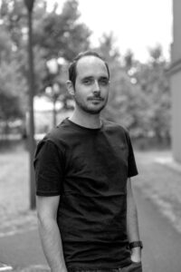 Portrait of Dieter Van Hoof standing outdoors, wearing a dark T-shirt, with a blurred green background.