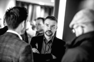 Tom Stroobants at a networking event, standing with arms crossed, in conversation with other attendees.