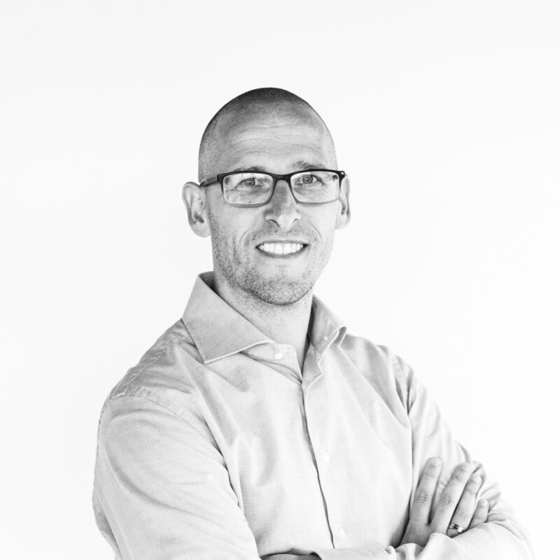 Portrait of Robert Buisman smiling with arms crossed, wearing glasses and a light shirt on white background.
