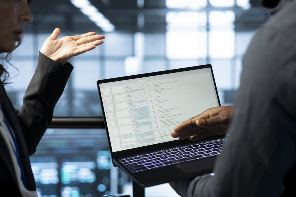 Two professionals discussing code on a laptop in a modern data center, collaborating on data architecture and AI infrastructure.